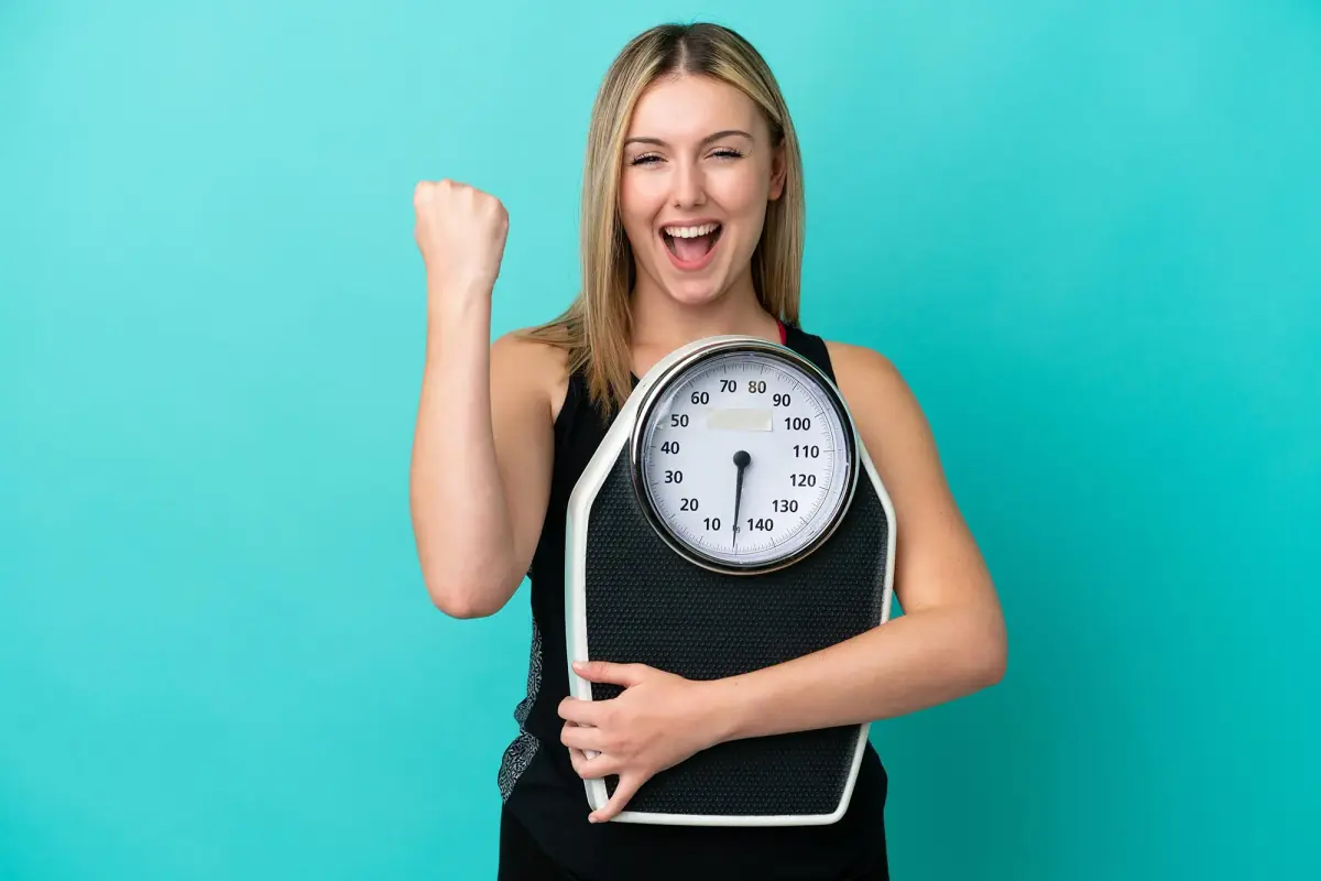 JellyThin customer review and success story. A happy, smiling woman holding a weighing scale, celebrating natural fat burn and effective weight loss results in the USA.